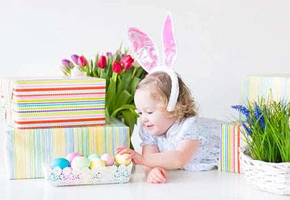 Little girl lying on her tummy with bunny ears and basket of Easter eggs