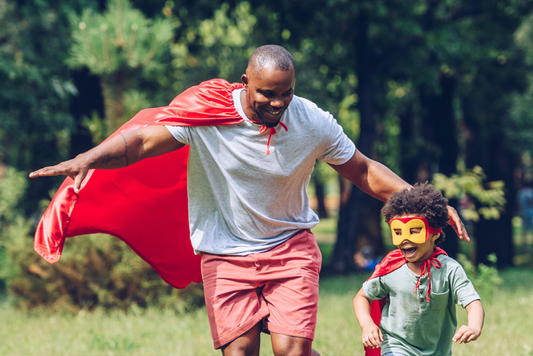 Father and child playing in a park with superhero cape