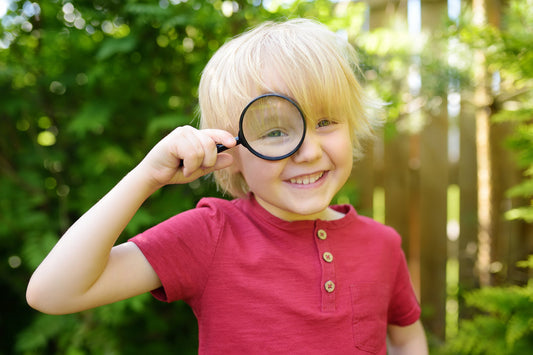 Boy looking into magnifying glass to find out summer camp things