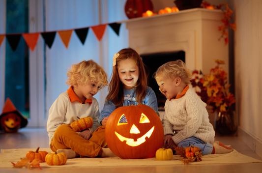 three kids sitting around a jack o lantern and smiling, celebrating halloween in sweaters