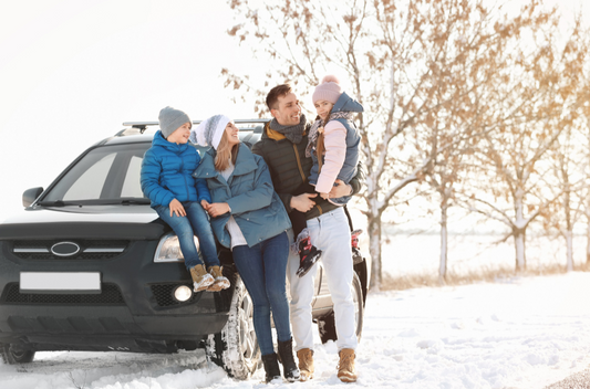 A man, woman and two children in winter clothes sitting on the front side of a car, smiling