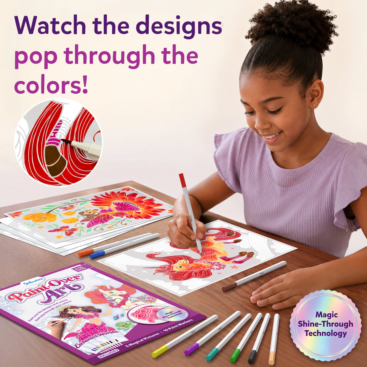 A young girl seated at a wooden table smiling while coloring Paint-Over Art sheets with markers; completed bright floral and fantasy designs visible, open kit box and scattered markers around, text reads Watch the designs pop through the colors, Magic Shine-Through badge shown.