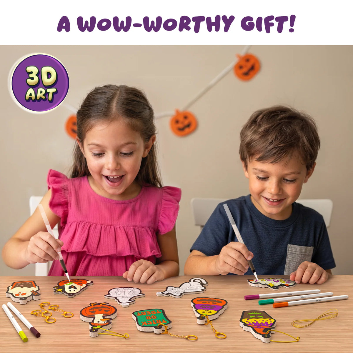 Excited girl in a pink dress and smiling boy in a navy T-shirt using water pens on colored Aqua Puffs at a wooden table with markers, gold keychains, string and Halloween foam shapes like Trick or Treat and Spooky signs, under a pumpkin garland. Text: A wow-worthy gift, with a 3D Art badge.
