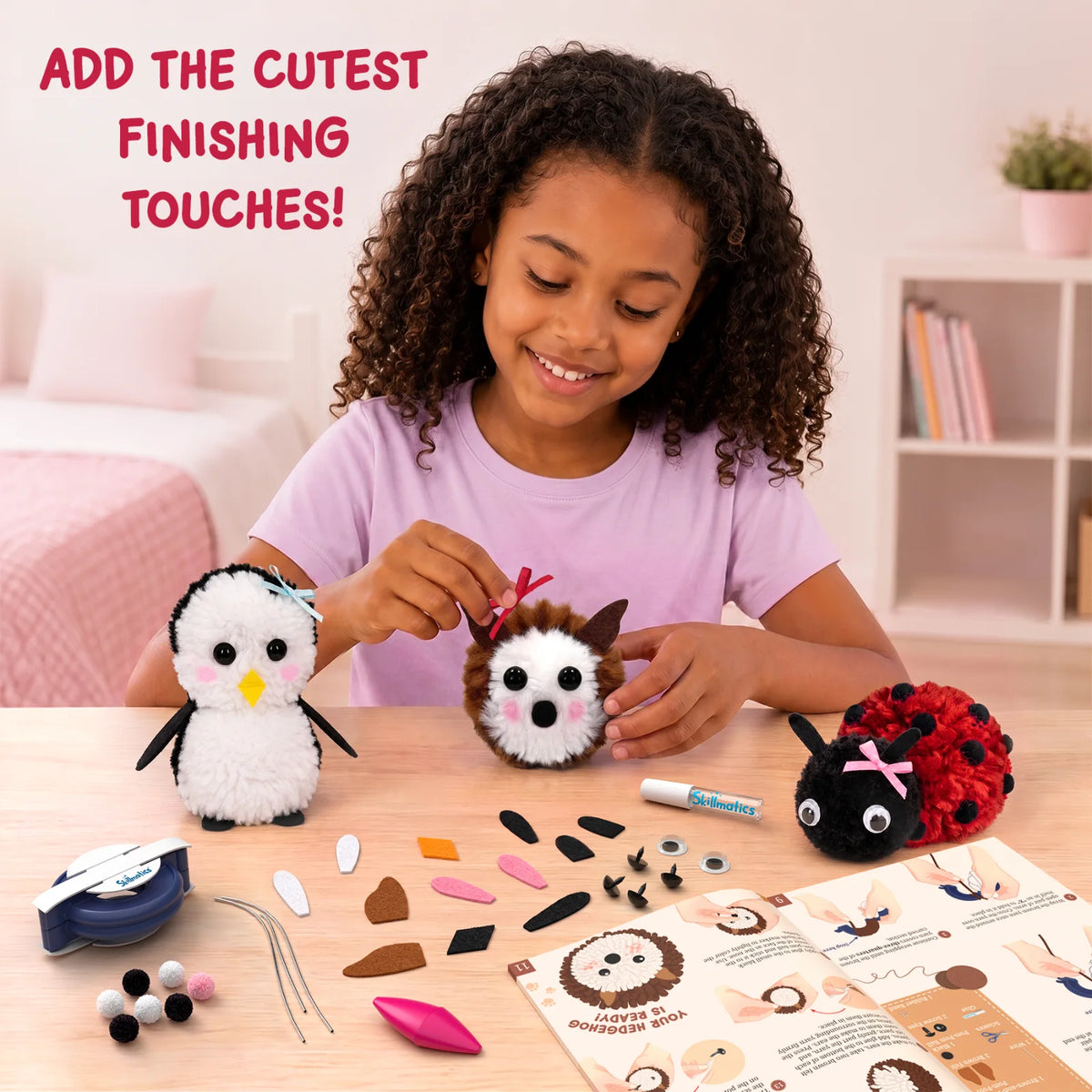 A smiling child decorates three Skillmatics PomPals yarn animals, including a penguin, hedgehog and red-and-black ladybug. The table displays a pom-pom maker, glue, yarn balls, felt shapes, googly eyes, wires, pom-poms and an illustrated instruction guide.